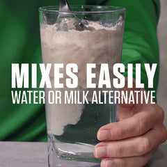 Vaso con Dymatize Vegan Plant Protein Vainilla Suave mezclado en agua, bebida proteica lista